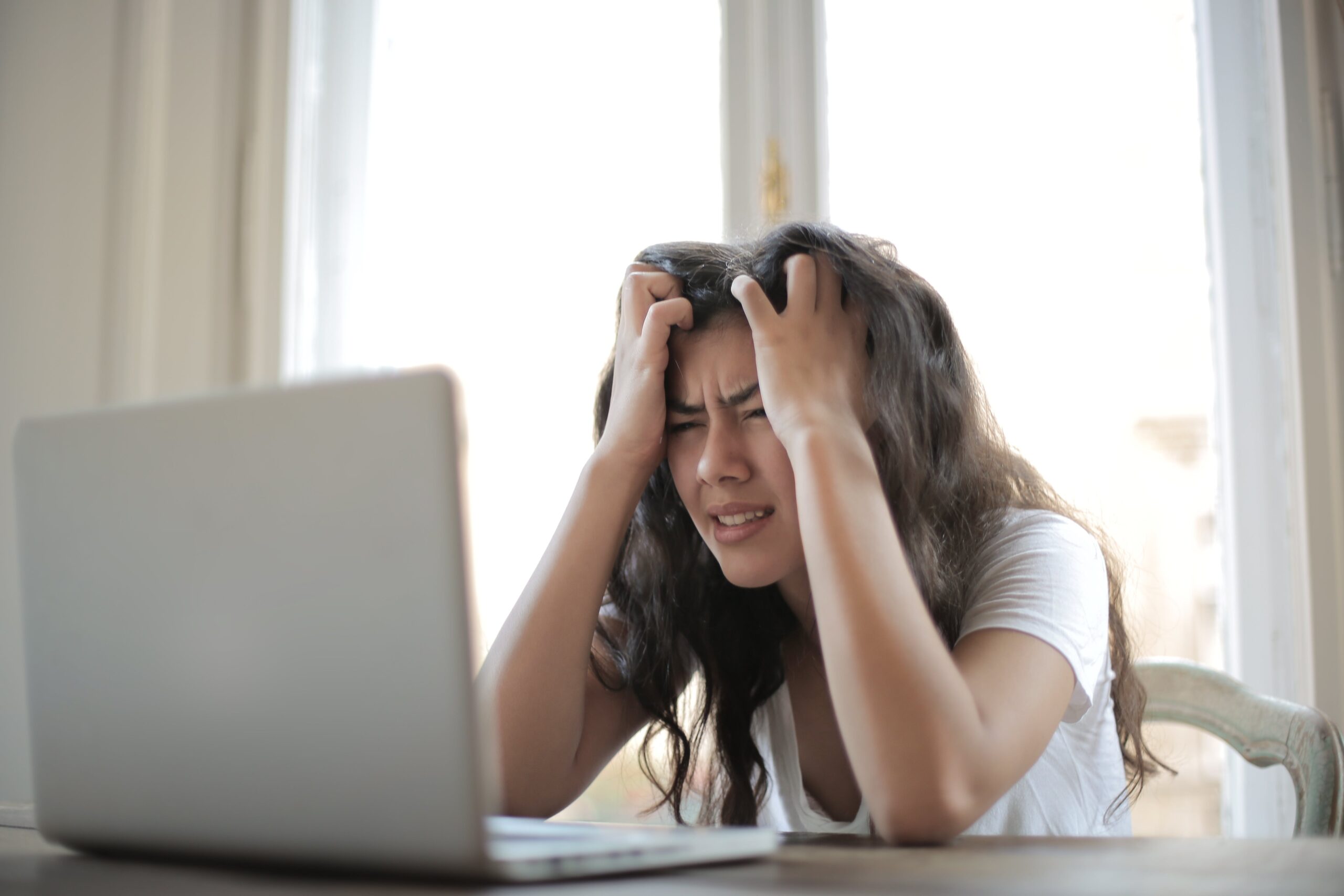stressed woman sits in front of a computer screen with hands in hair