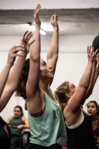 Woman in teal shirt holds arms overhead after throwing ball