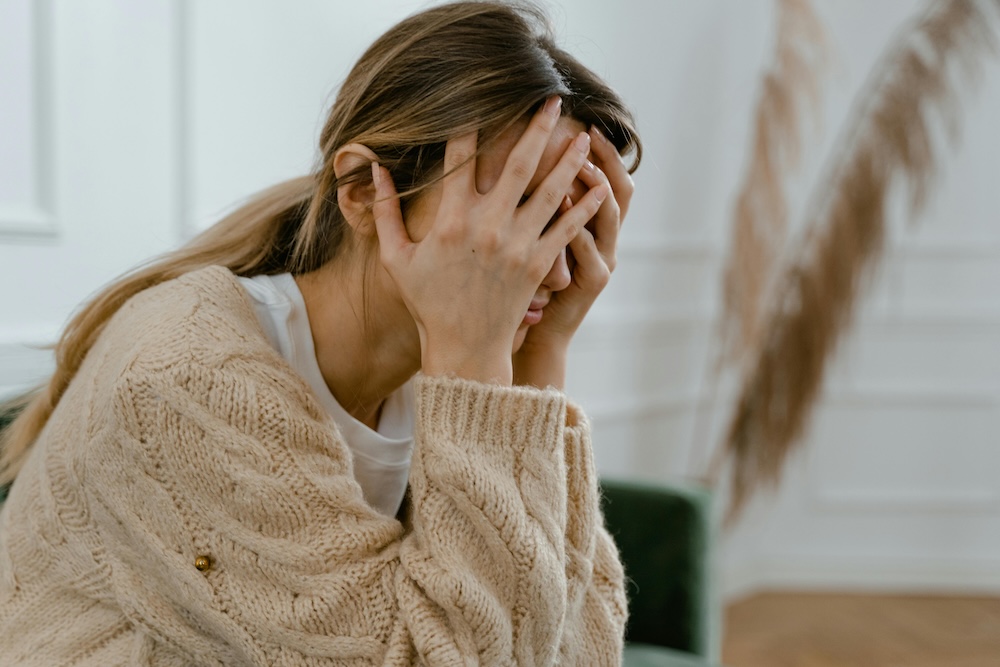 Hypermobile woman sits with her head in her hands due to a headache from generalised joint hypermobility