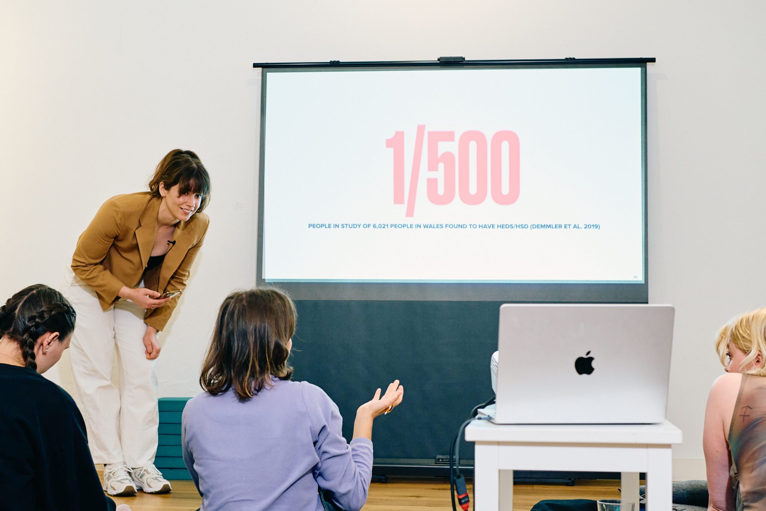 Hypermobility specialist osteopath answers question asked by audience member while standing in front of slide with text reading "1/500" on it