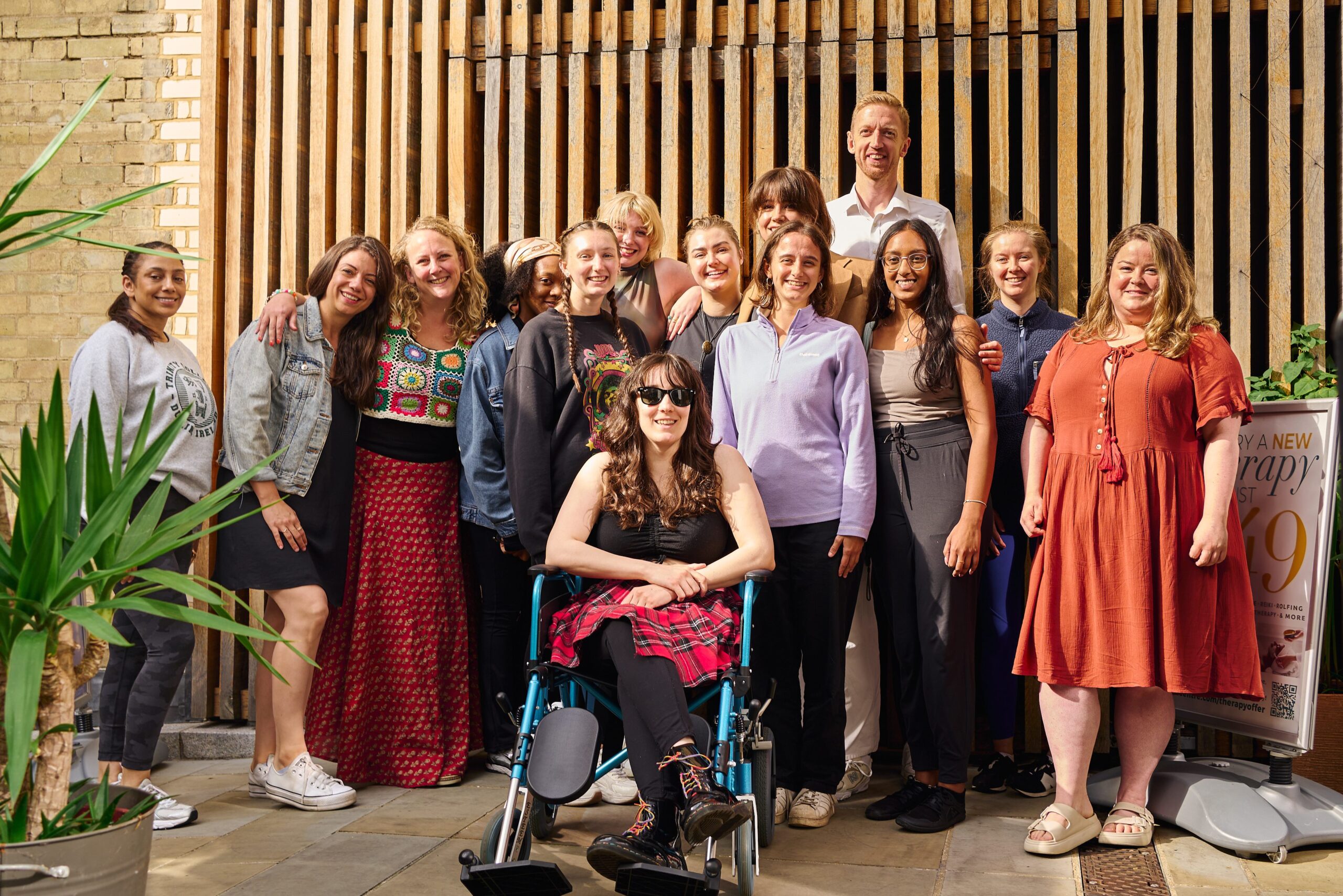 Workshop group stands outside in sunshine in front of a wooden fence