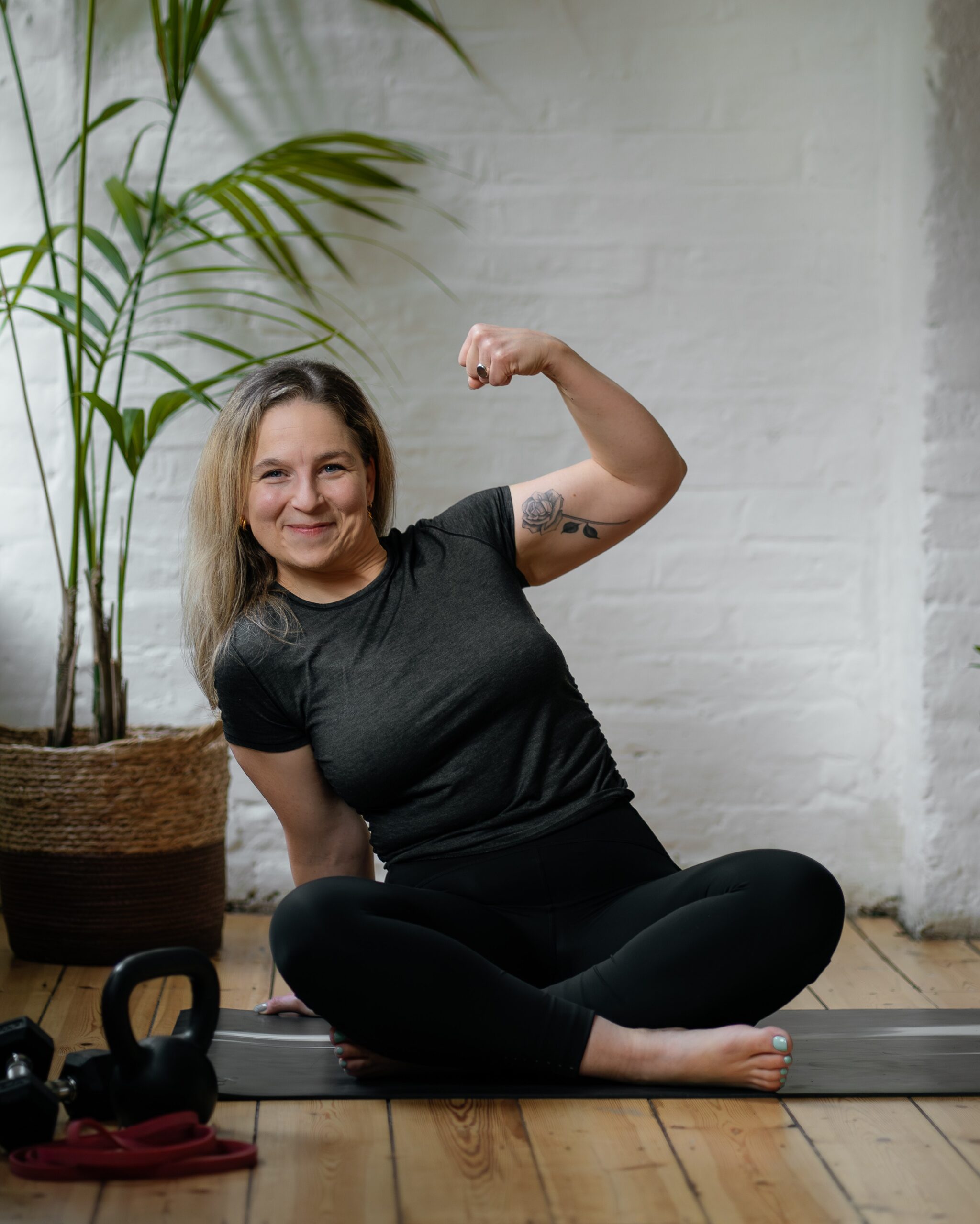 Hypermobility Movement Coach sits cross legged on the floor while flexing her left arm