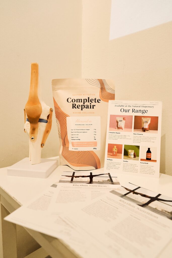 A package of Rhythm Nutrition protein power is positioned on a white desk with a knee joint and promotional flyers beside it. 